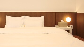 Una cama bien hecha con sábanas blancas, una mesita de noche con una lámpara y una caja de pañuelos.