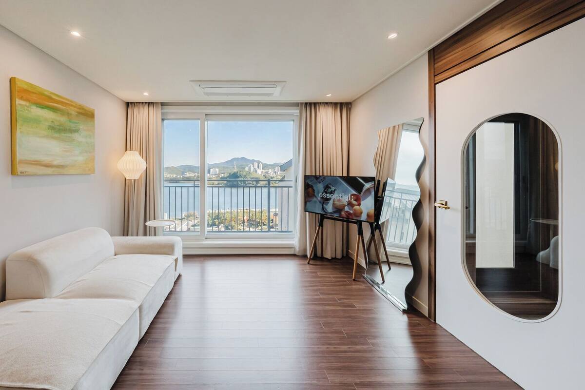 Ein modernes Hotelzimmer mit Sofa, Fernseher, einem Gemälde und einem Balkon mit Blick auf die Stadt.