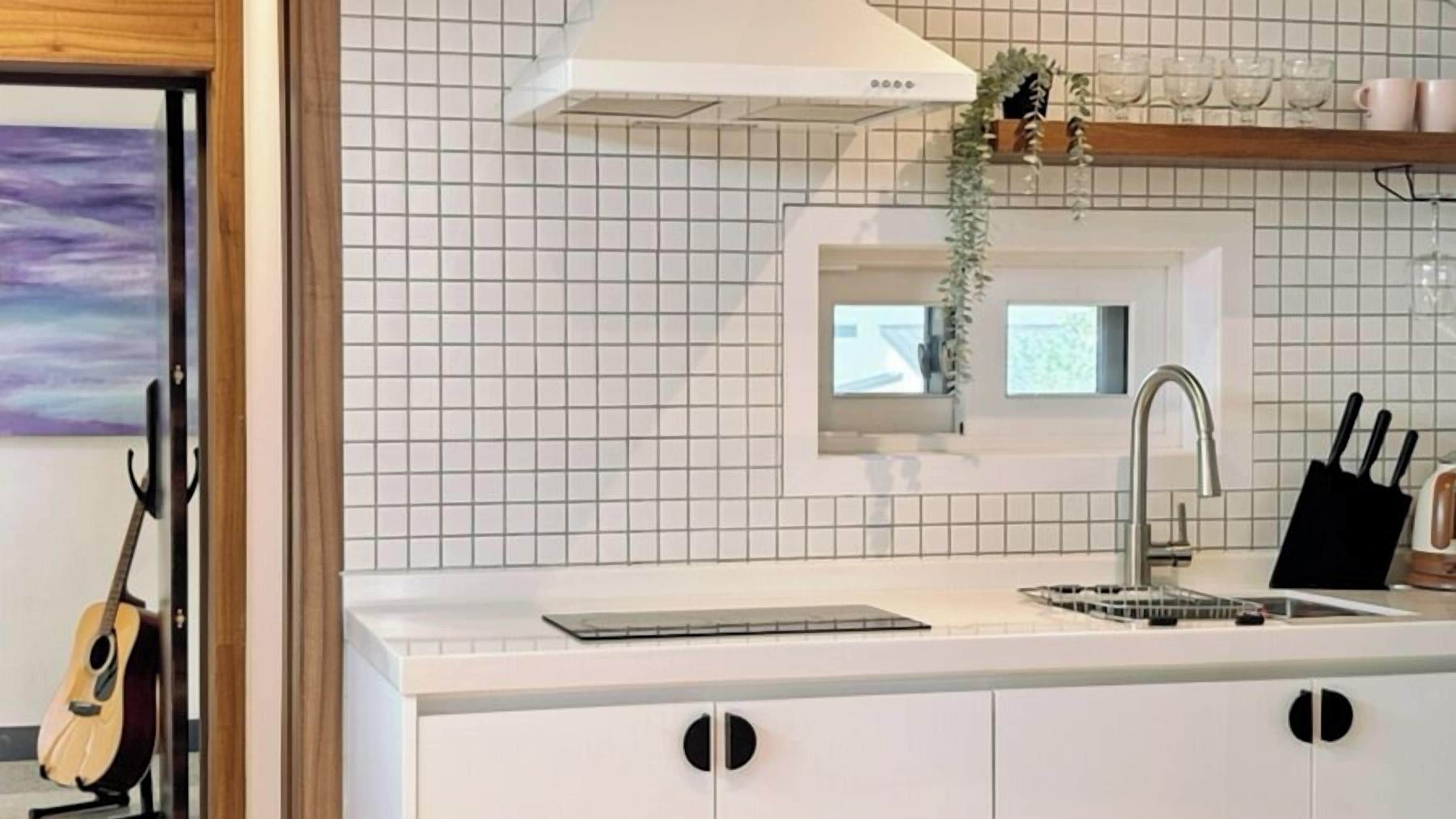 A kitchen with white tiled backsplash, a stainless steel sink, and a knife block on the countertop.