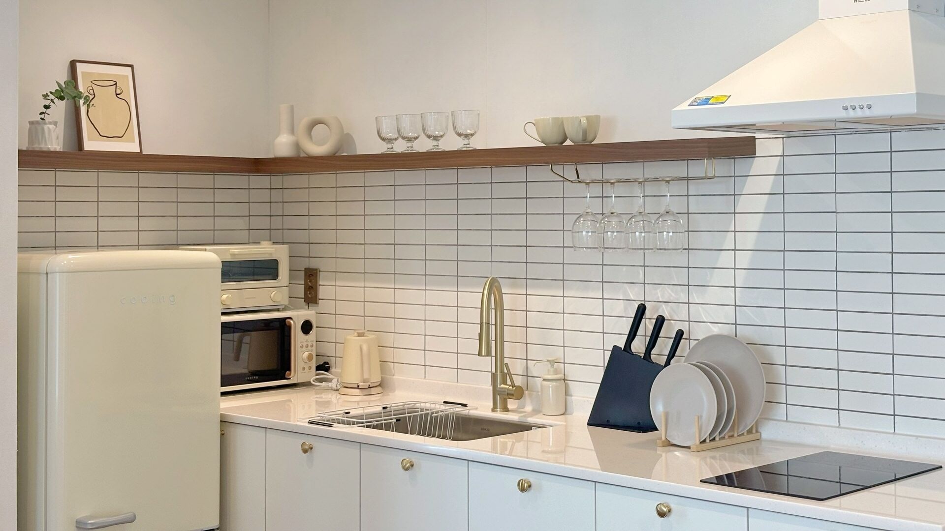 A modern kitchen with white cabinetry, a built-in oven, a microwave, a sink with a faucet, and a dish rack.