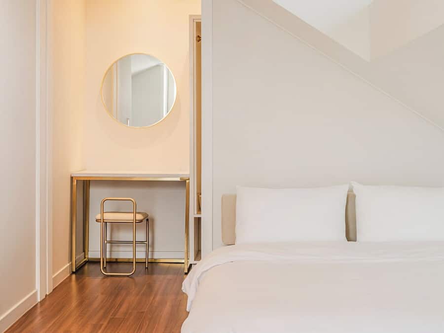 Ein Schlafzimmer mit einem Bett, einem Nachttisch, einem Sessel, einem Spiegel und einer Tür.