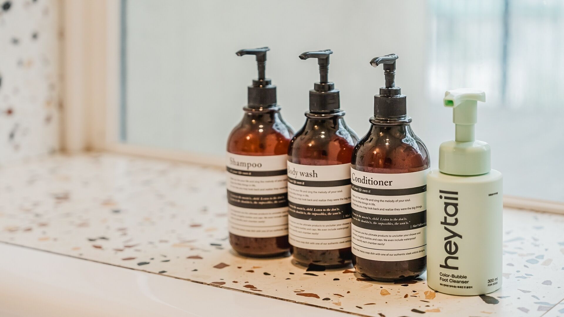 Four bottles of personal care products on a speckled countertop.