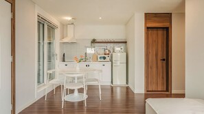 A compact kitchen with white appliances, a dining table with chairs, and a wooden door. - Chuncheon Rehouse (Chuncheon)