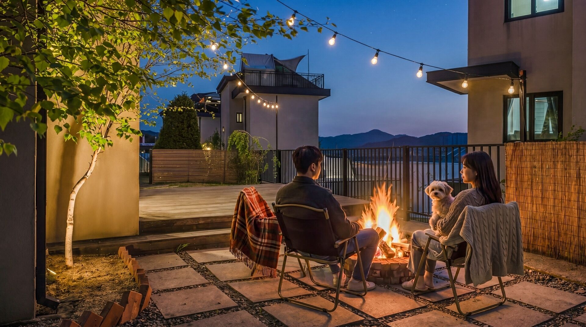 An outdoor seating area with a fire pit, surrounded by a patio with stone tiles and a view of a modern building.