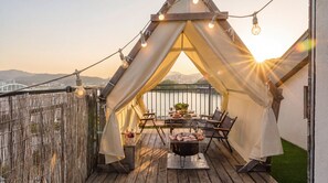 A rooftop terrace with a tent, outdoor seating, a grill, and string lights.