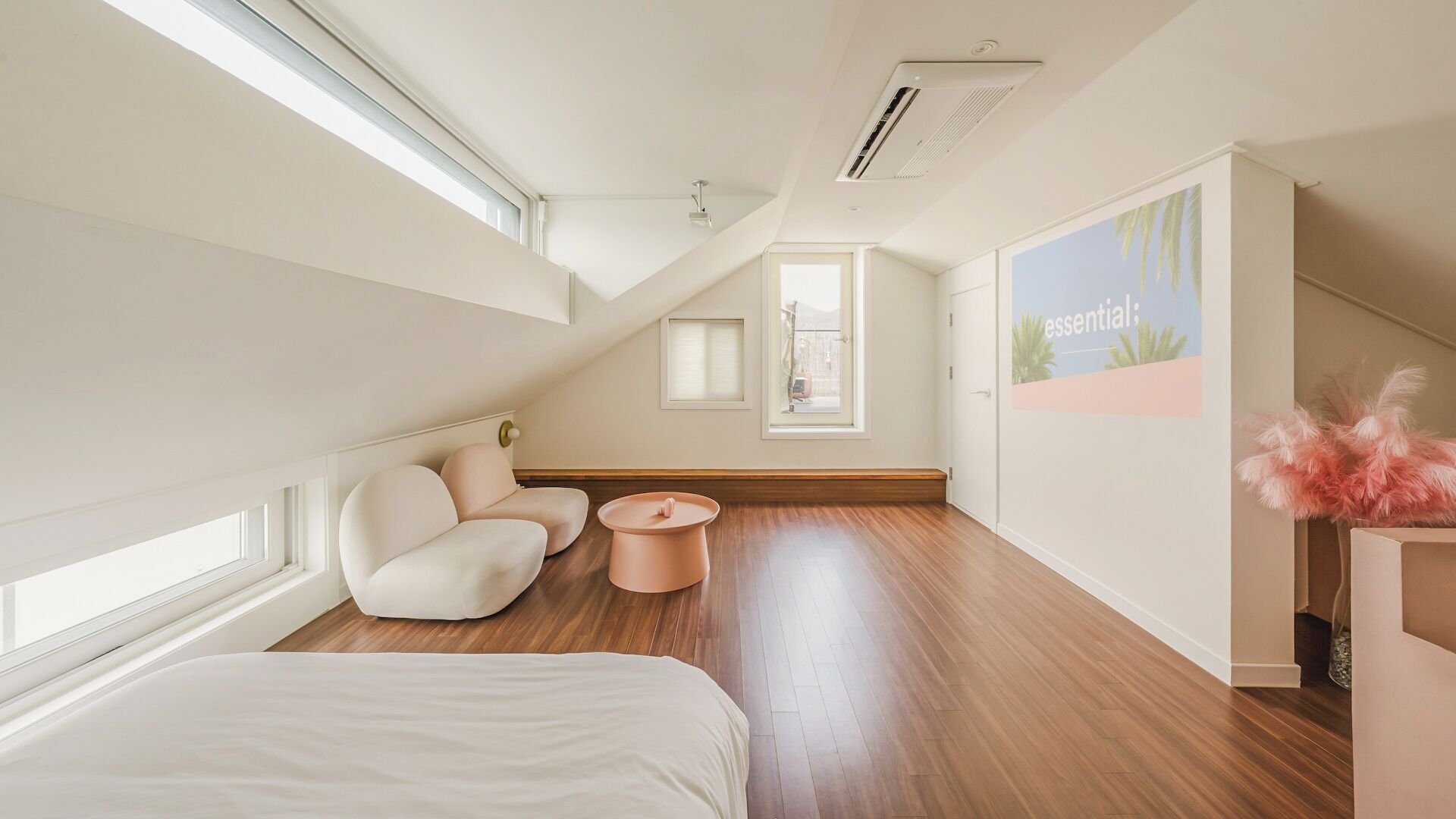 A modern bedroom with a sloped ceiling, a bed, a seating area with a table, and a large window.