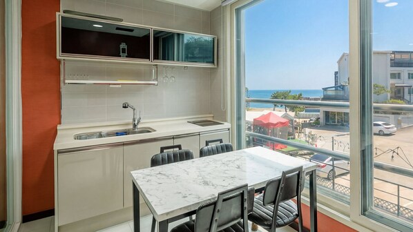 A modern kitchen with a marble countertop, a sink, and cabinets. There is a dining area with a table and chairs. - Daebudo The Habitch Spa Pension (Ansan)