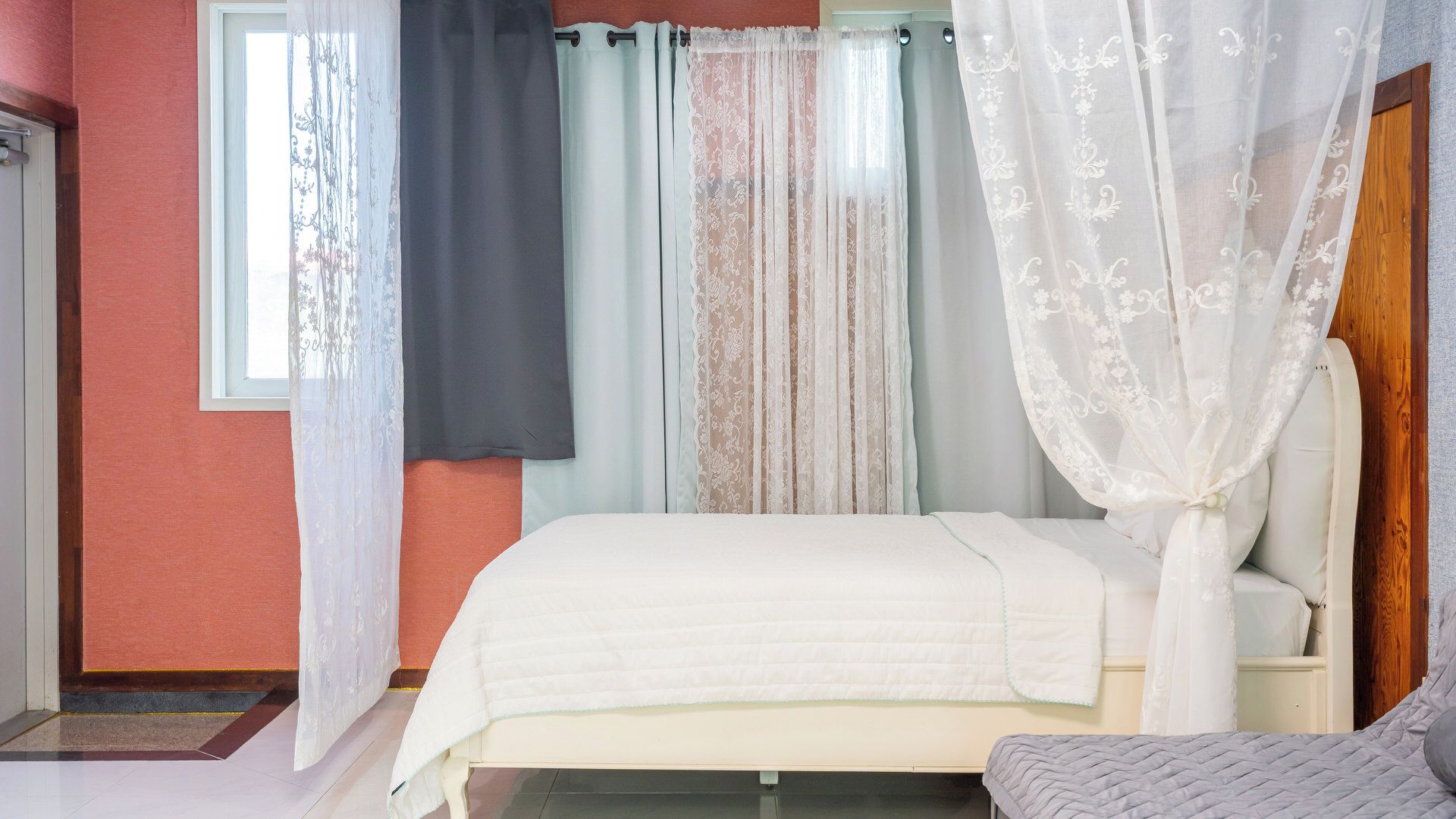 A bedroom with a bed, a nightstand, a chair, and a window with curtains.