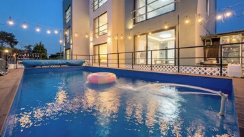 Una piscina con fuente, rodeada por una terraza y un edificio con amplios ventanales.