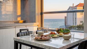 Una mesa de comedor con diversos platos, un tazón de arroz y vistas al mar a través de un ventanal grande.