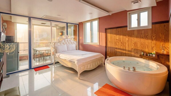 A bedroom with a large bed, a glass door leading to a balcony, a wooden wall, and a large bathtub.
