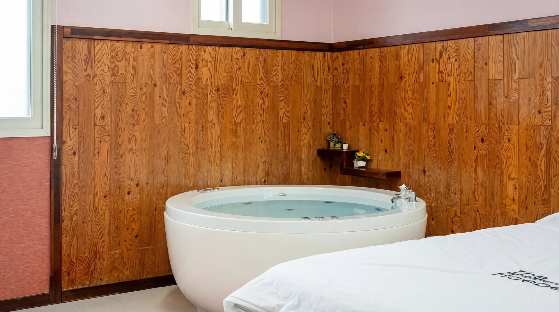 Een hoek slaapkamer met een houten paneelwand, een groot bad en een wit bed.