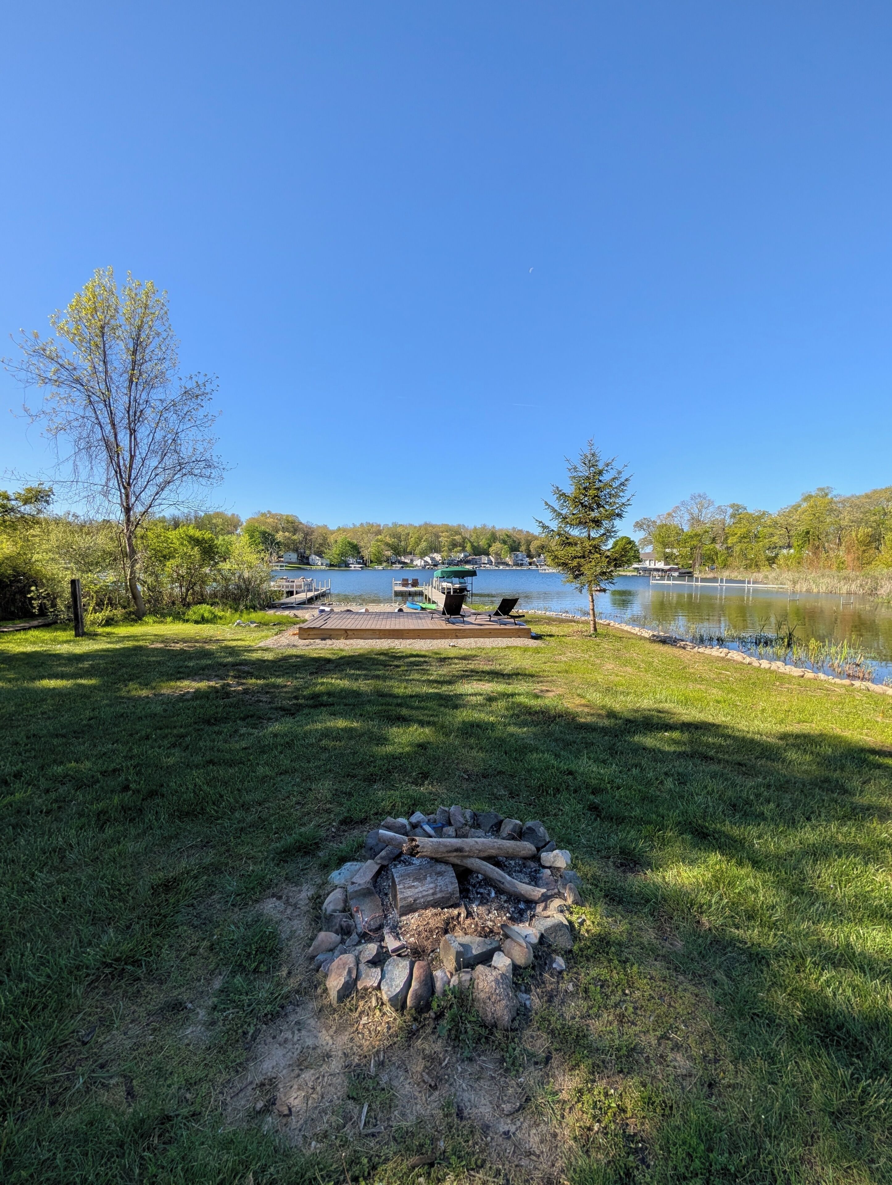 A lakeside camping area with a fire pit, dock, and boats.