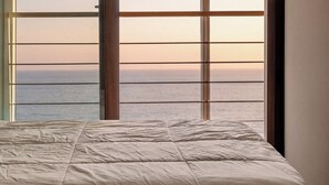 A bed with a white duvet in a room with a large window overlooking the sea. - Geoje Pings Pet-friendly Pension (Geoje)