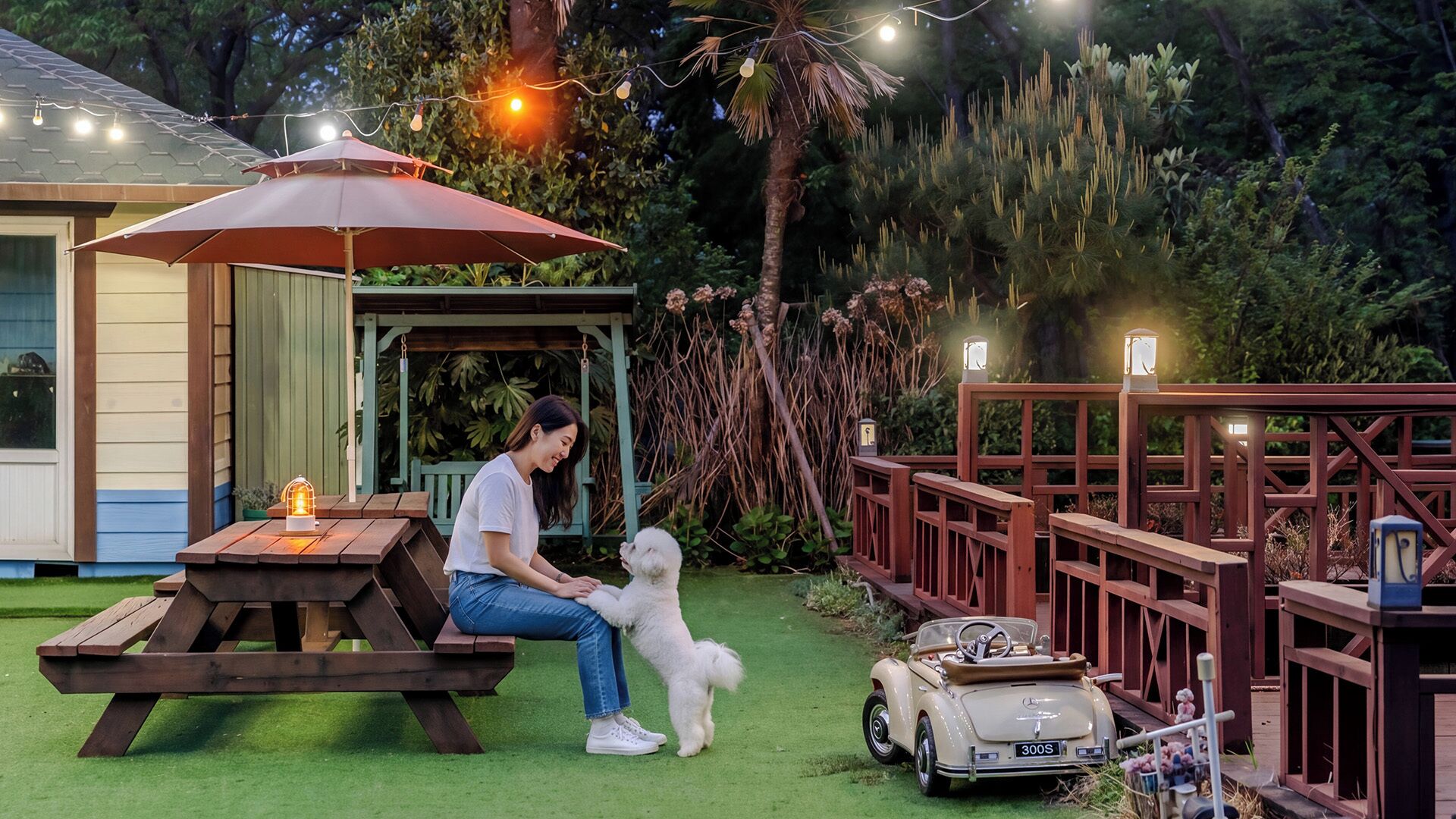 Una mesa de picnic, un perro pequeño y un coche antiguo en un patio trasero.