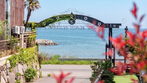 A coastal entrance with a metal archway, a stone wall, and a view of the sea. - Geoje Pings Pet-friendly Pension (Geoje)