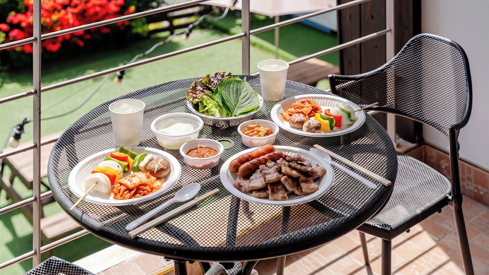 A round metal table with various dishes and drinks, surrounded by chairs on a balcony.