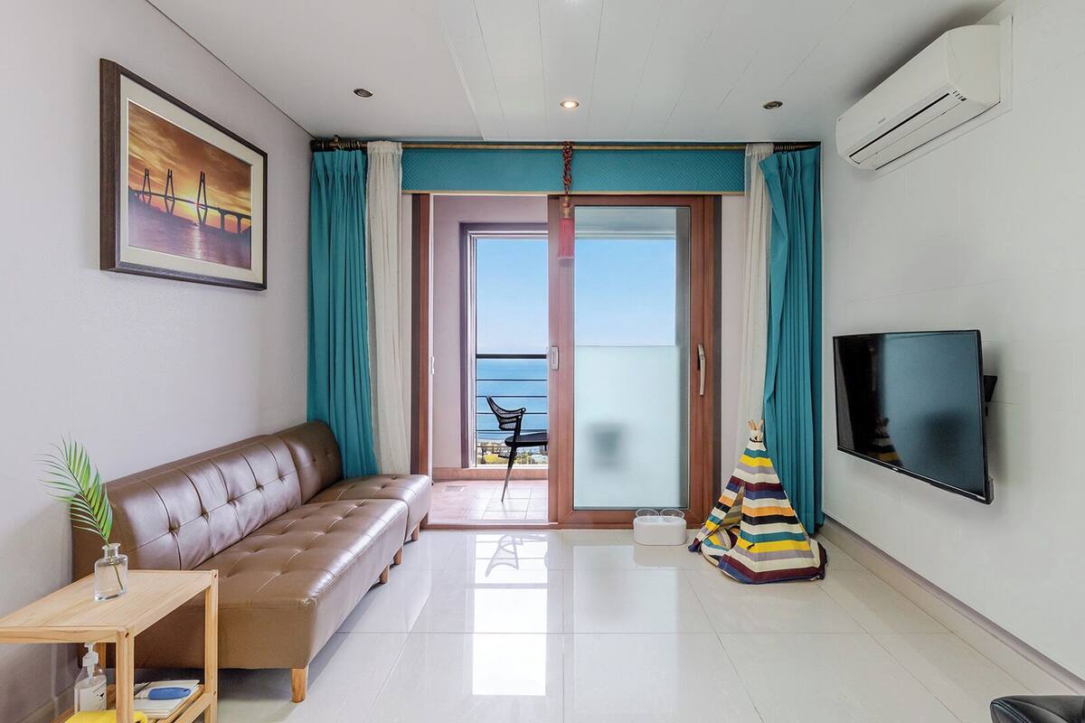 Una sala de estar moderna con un sofá, un televisor y vista al mar a través de un ventanal corredero.