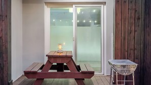 A wooden picnic table with a lantern and grill on a deck.