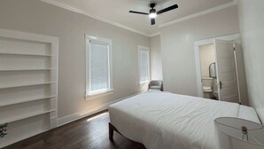 Un dormitorio con cama, ventilador de techo, ventana, silla y espejo.