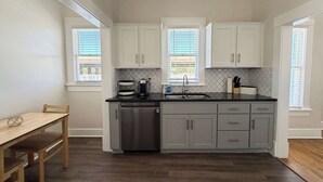 Una cocina compacta con armarios blancos, lavavajillas, fregadero y encimera con cafetera.