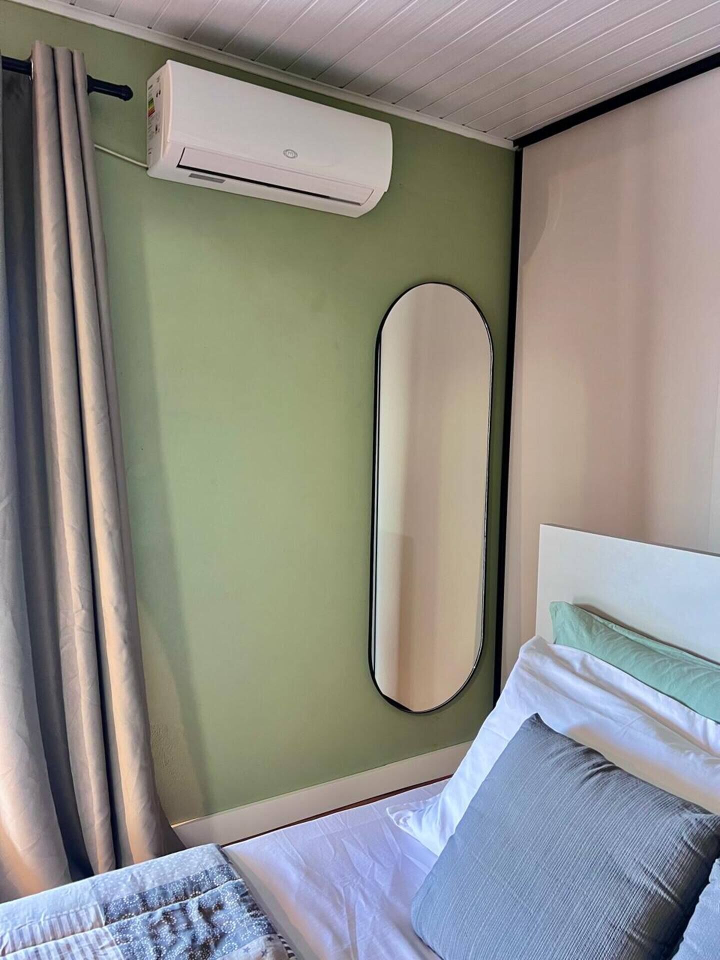 A room with a bed, a wall-mounted air conditioner, a large mirror, and a curtain.
