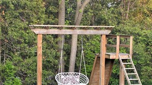 A wooden swing set with a hanging chair and a ladder. - Family Friendly Cottage close to beach and main strip. (Grand Bend)