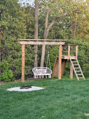 A wooden swing set with a hanging chair and a ladder.