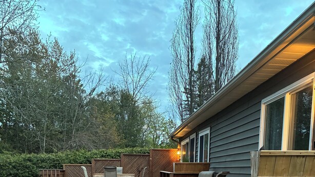 A deck with a built-in table and chairs, surrounded by a wooden fence, and a house with a window to the right. - Family Friendly Cottage close to beach and main strip. (Grand Bend)