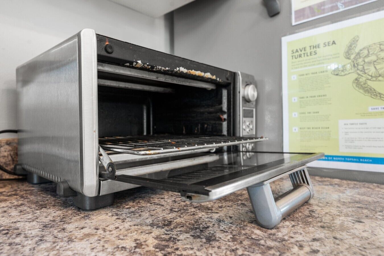 A stainless steel toaster oven with a tray rack, placed on a granite countertop.