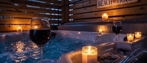 Uma banheira de hidromassagem com velas e copos de vinho, identificada como 'BEACH HOUSE'.