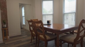 A dining area with a wooden table and chairs, a potted plant, and a window with blinds.