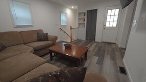 A living room with a sofa, a coffee table, and a staircase leading to a door. - Main Haven- Spacious 4BR Retreat 9 min to All star Village 21 min to Cooperstown (Oneonta)