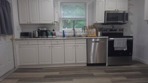 A modern kitchen with white cabinets, stainless steel appliances, a dishwasher, and a window with blinds. - Main Haven- Spacious 4BR Retreat 9 min to All star Village 21 min to Cooperstown (Oneonta)