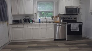 A modern kitchen with white cabinets, stainless steel appliances, a dishwasher, and a window with blinds.