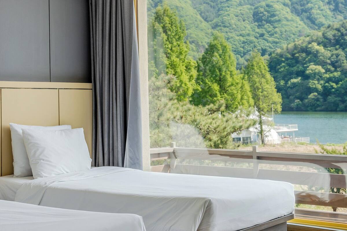 A hotel room with a bed, a window with a view of a lake and forest.