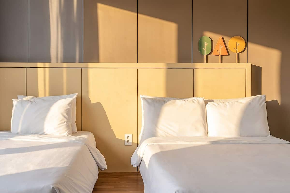 A hotel room with two beds, a wooden floor, and a wall with a geometric design.