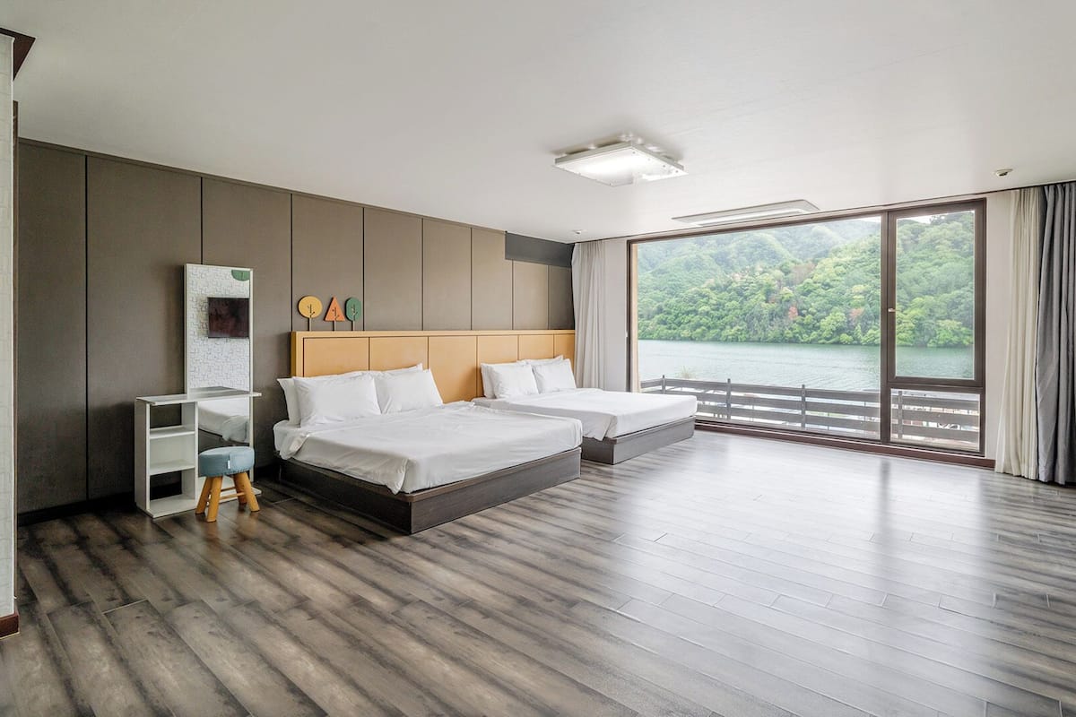 A modern hotel room with a large bed, a desk, and a view of a lake.