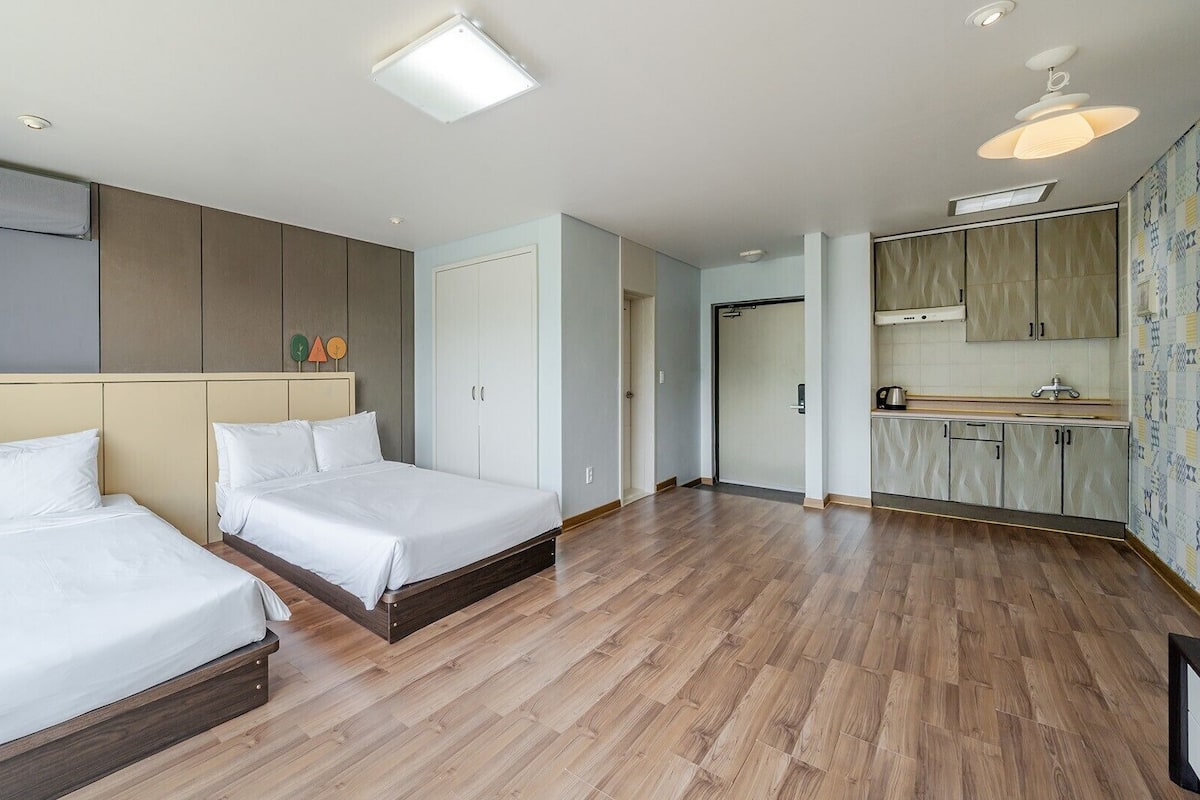 A hotel room with two beds, a kitchenette, and a bathroom.