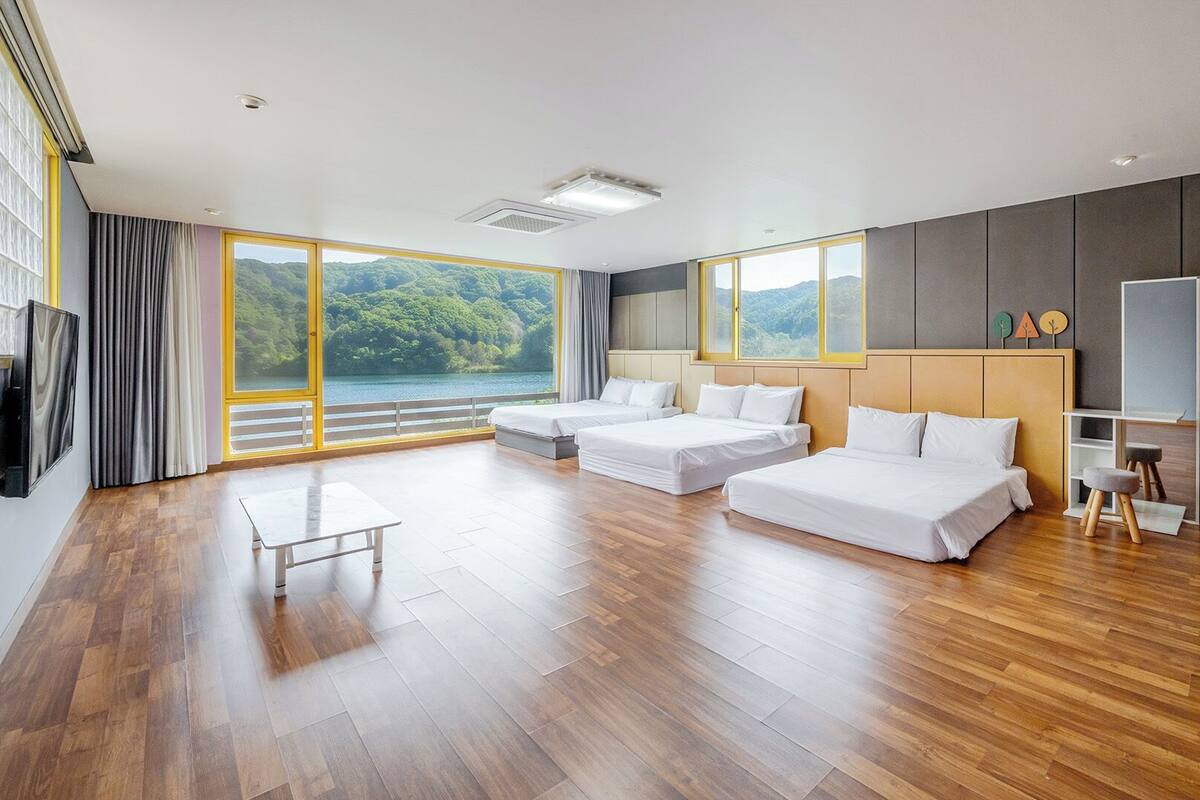 A modern hotel room with a large bed, a smaller bed, a desk, and a view of a lake.