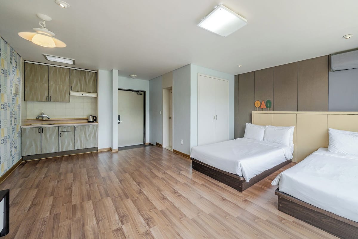 A hotel room with two beds, a kitchenette, and a bathroom.