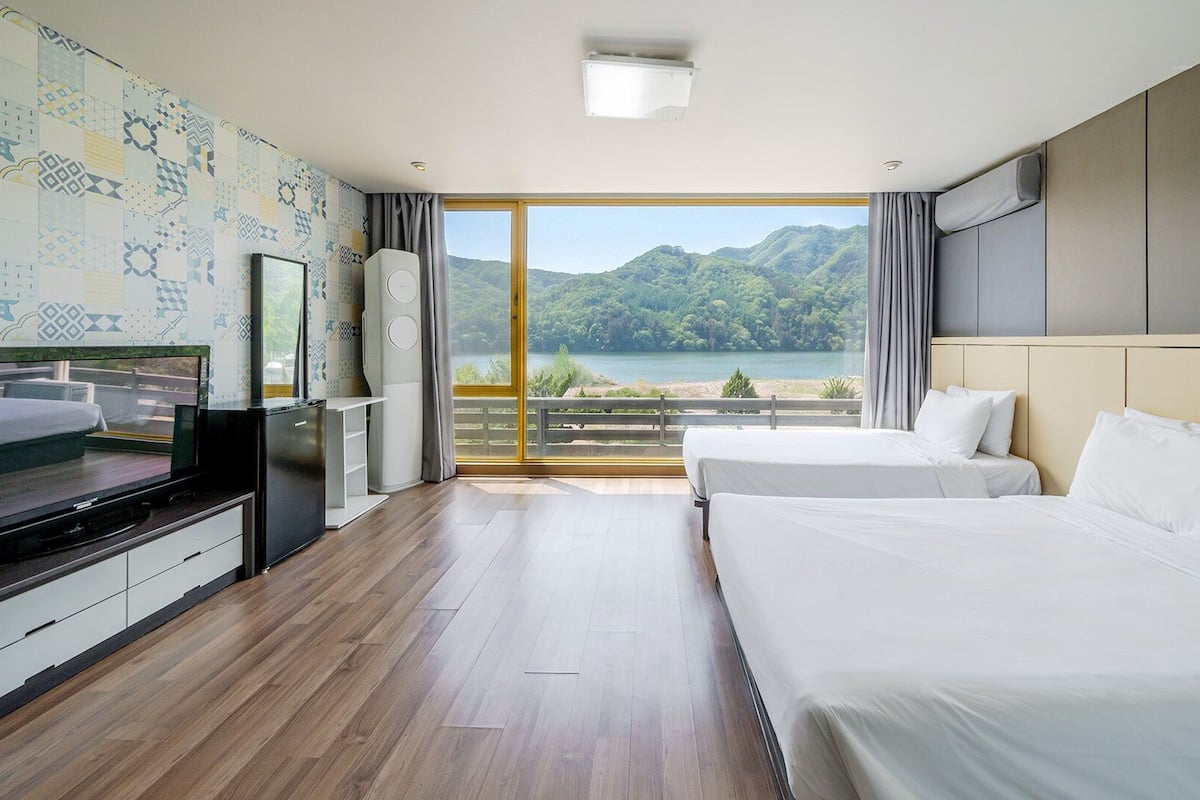 A hotel room with a large bed, a TV, a mini-fridge, and a view of a lake.