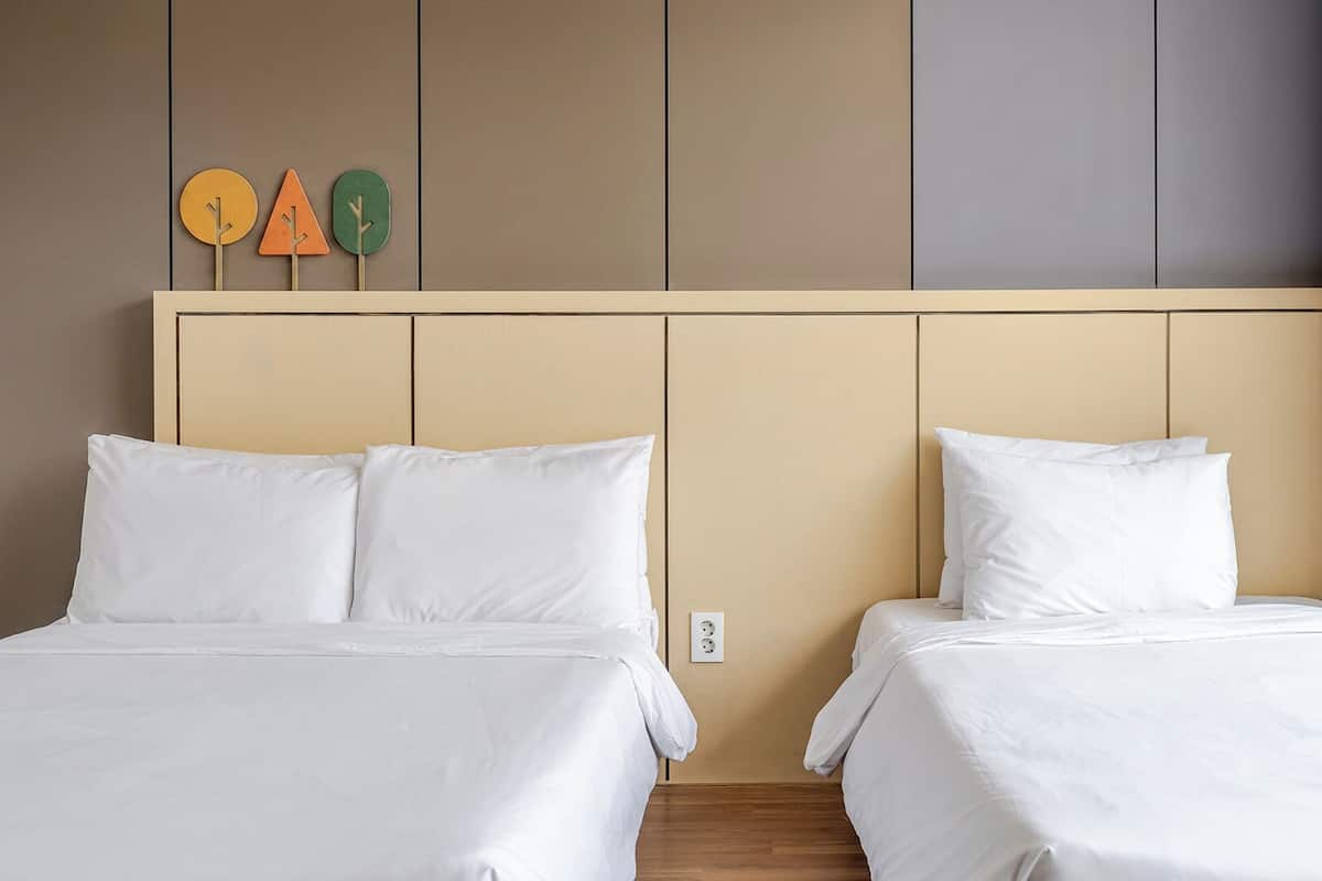 A hotel room with two beds, a neutral color scheme, and a simple decor including a wall-mounted clock and a small plant.