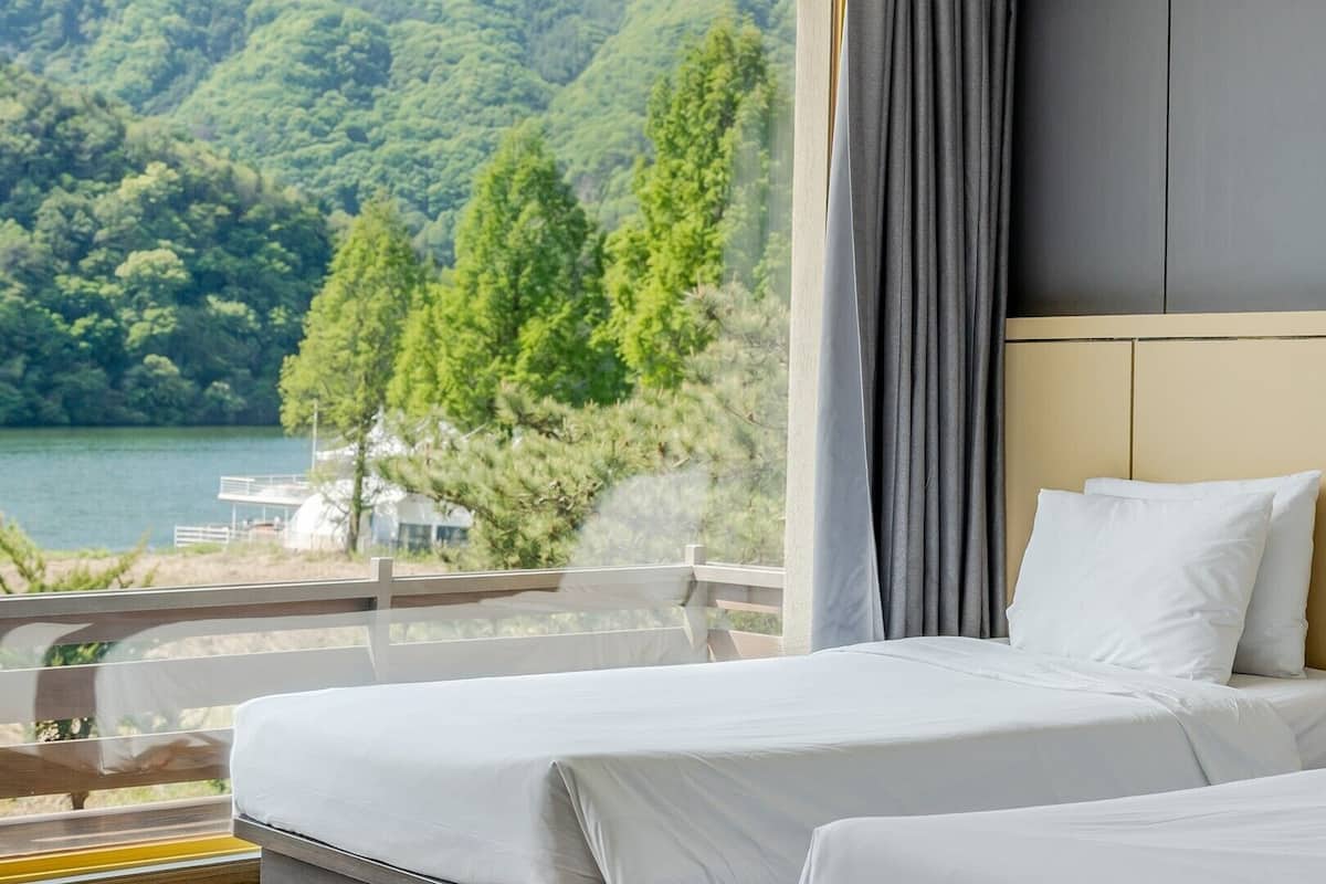 A hotel room with two beds, a view of a lake, and a balcony with a railing.