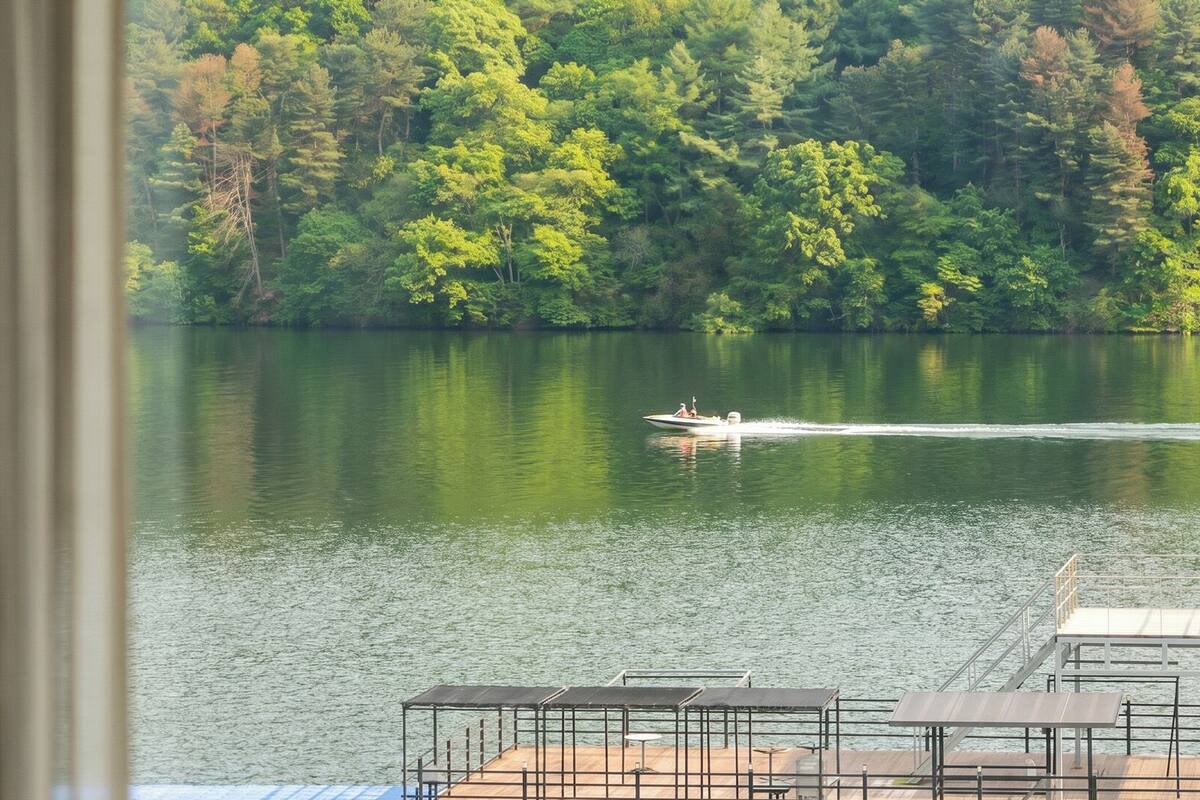 A boat on a calm lake with a dock and a forested shoreline.