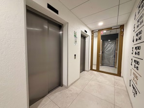 An interior corridor with an elevator, a door with a sign, and a wall with numbered signs. - Czysta Bright Studio (Wrocław)