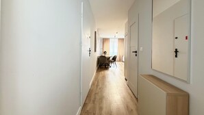 Un pasillo con suelo de madera, paredes blancas y puertas que dan a un comedor con mesa y sillas.