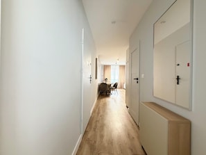 A hallway with wooden flooring, white walls, and doors leading to a dining area with a table and chairs. - Kłodzka Homely Apartment (Wrocław)