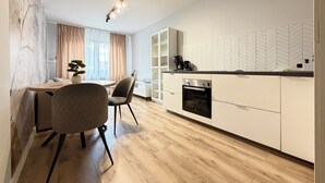 Una cocina moderna con horno integrado, una zona de comedor con una mesa redonda y sillas, y un ventanal con cortinas.