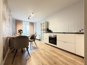 A modern kitchen with a built-in oven, a dining area with a round table and chairs, and a large window with curtains. - Kłodzka Homely Apartment (Wrocław)